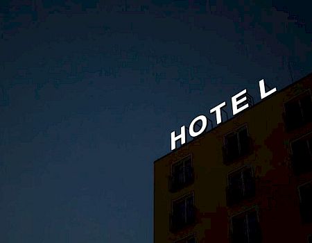 A building with a neon "HOTEL" sign, at night, missing the letter "T".