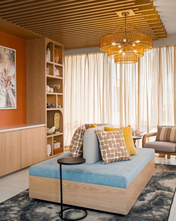 A modern living room with a wooden ceiling, artwork, comfy seating, warm lighting, plants, and sheer curtains enhancing the natural light.