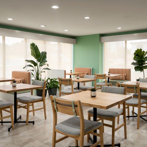 The image shows a bright, modern cafe with wooden tables, chairs, plants, and striped cushioned benches, featuring large windows and soft lighting.
