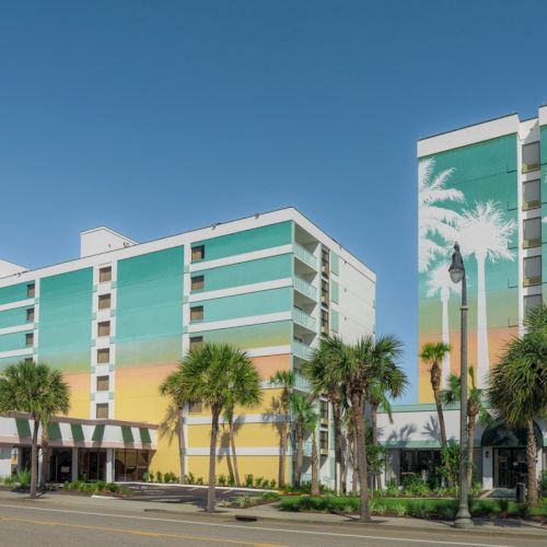 Colorful hotel building with palm trees and painted mural walls under a clear blue sky.