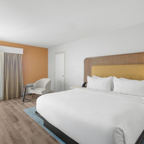 A modern hotel bedroom with a king bed, bedside lamps, and a balcony view of the ocean.