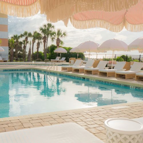 A serene poolside scene with lounge chairs, umbrellas, and palm trees, reflecting a peaceful, vacation-like atmosphere.