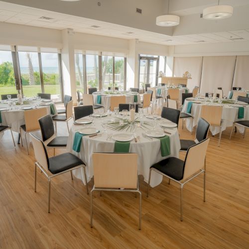 The image shows a spacious banquet hall with round tables set for a meal, featuring white tablecloths and green accents.