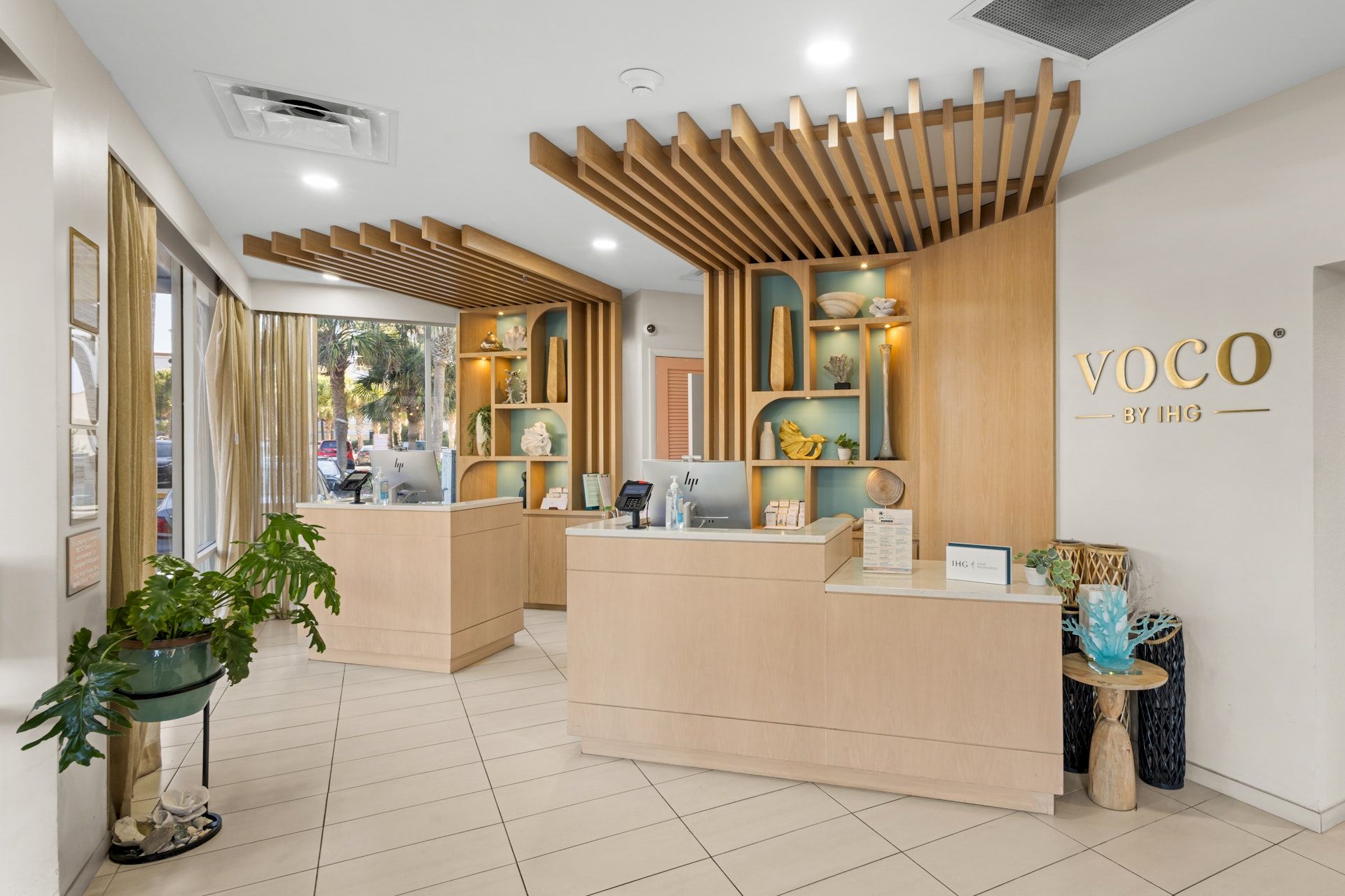 Bright hotel reception with wooden slats and a front desk, and a &ldquo;voco by IHG&rdquo; sign on the wall.