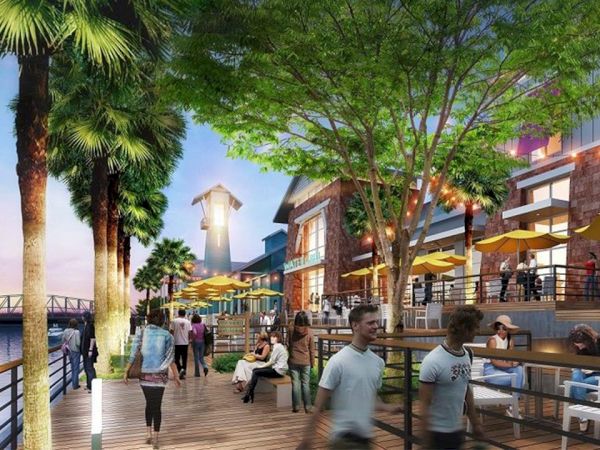 A lively waterfront boardwalk with people, palm trees, outdoor dining under yellow umbrellas, and boats on the water.