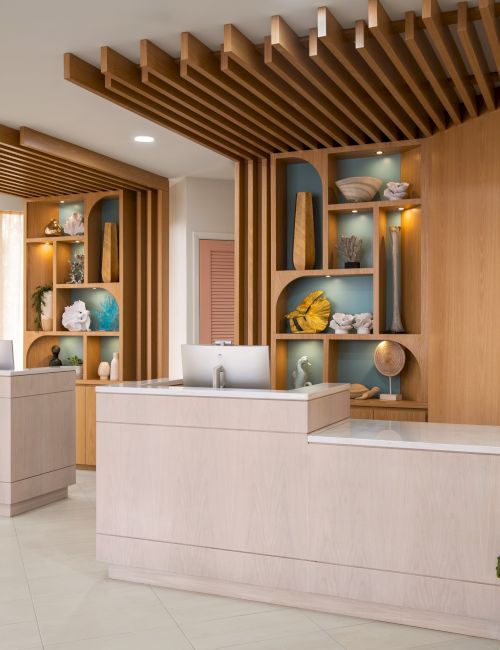 A hotel reception area with two desks, decorative shelves, and warm wood accents; a "Voco by IHG" sign is on the wall.
