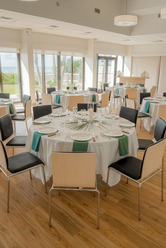 A bright banquet hall set for a formal dinner with tables, place settings, and green napkins.