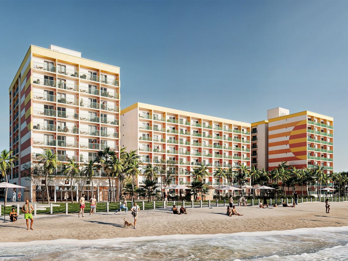 A colorful beachfront hotel with people enjoying a sunny day on the beach, palm trees lining the promenade.