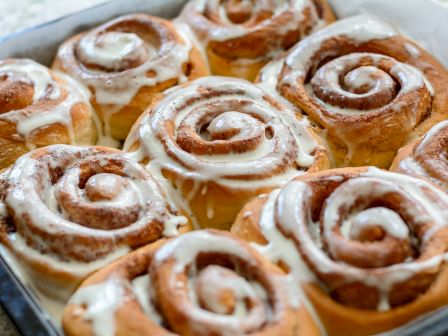 The image shows a tray of freshly baked cinnamon rolls topped with white icing, neatly arranged and ready to be served.