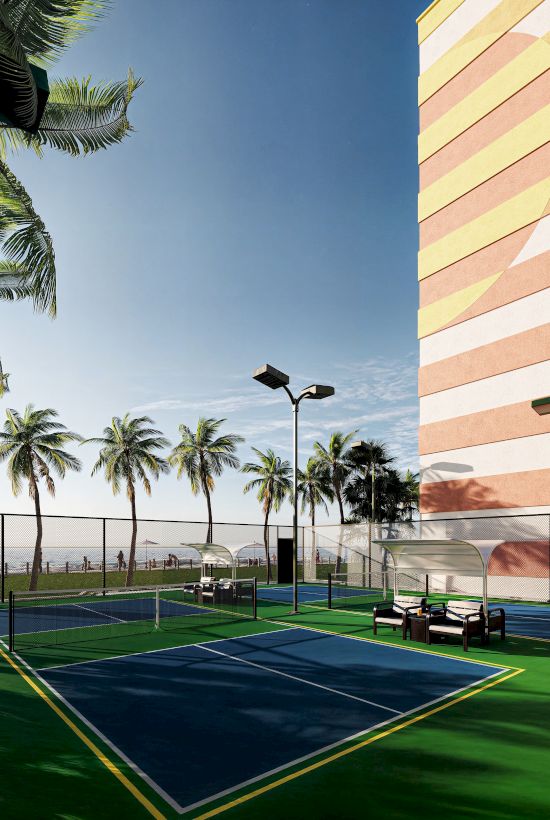 Tennis courts with seating, framed by palm trees and a multicolored building, under a clear blue sky.