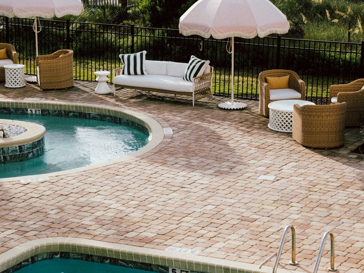 A poolside scene with two swimming pools, lounge chairs, and umbrellas near a beach, creating a relaxing and scenic atmosphere.