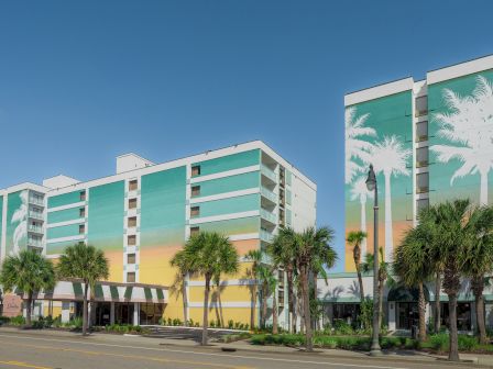 A multi-story building with palm tree murals and real palm trees lining the street on a clear day.