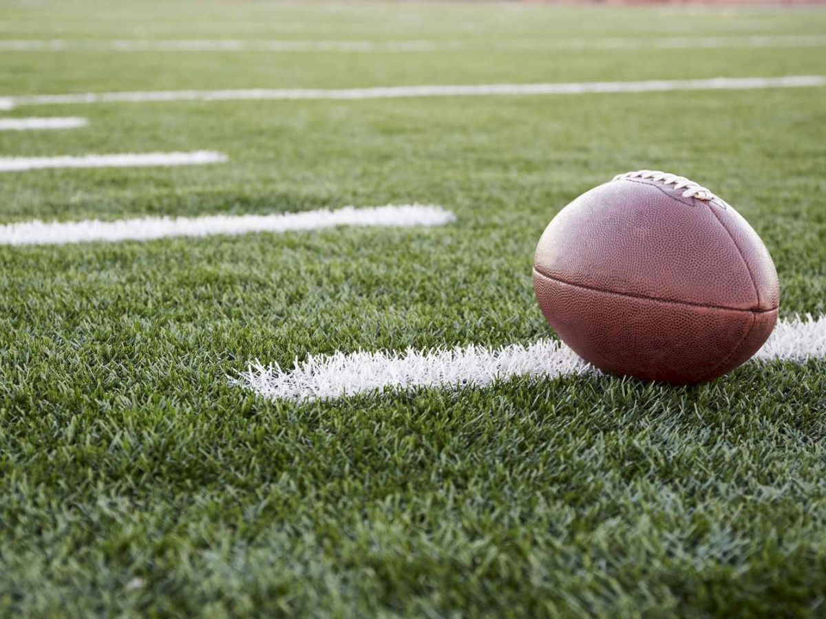 A close-up of a football on a green turf field, resting near white yard lines, ready for play.