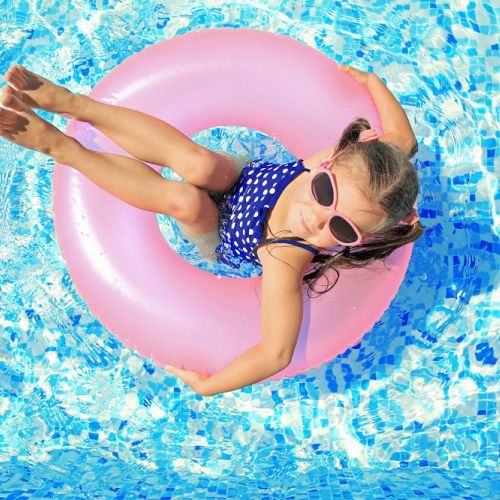 A person lounging on a pink inflatable ring in a swimming pool, sunny day.